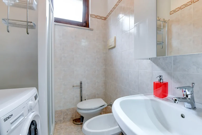 Bright bathroom with sink, toilet, bidet, shower and washer near Lago di Garda.