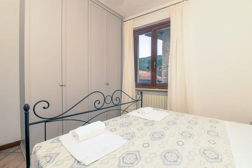 Cozy bedroom with iron bed, wardrobe, towels and window view near Lago di Garda
