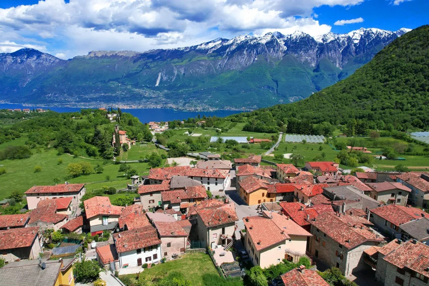Hill village with terracotta roofs, green fields and snowy peaks by Lake Garda